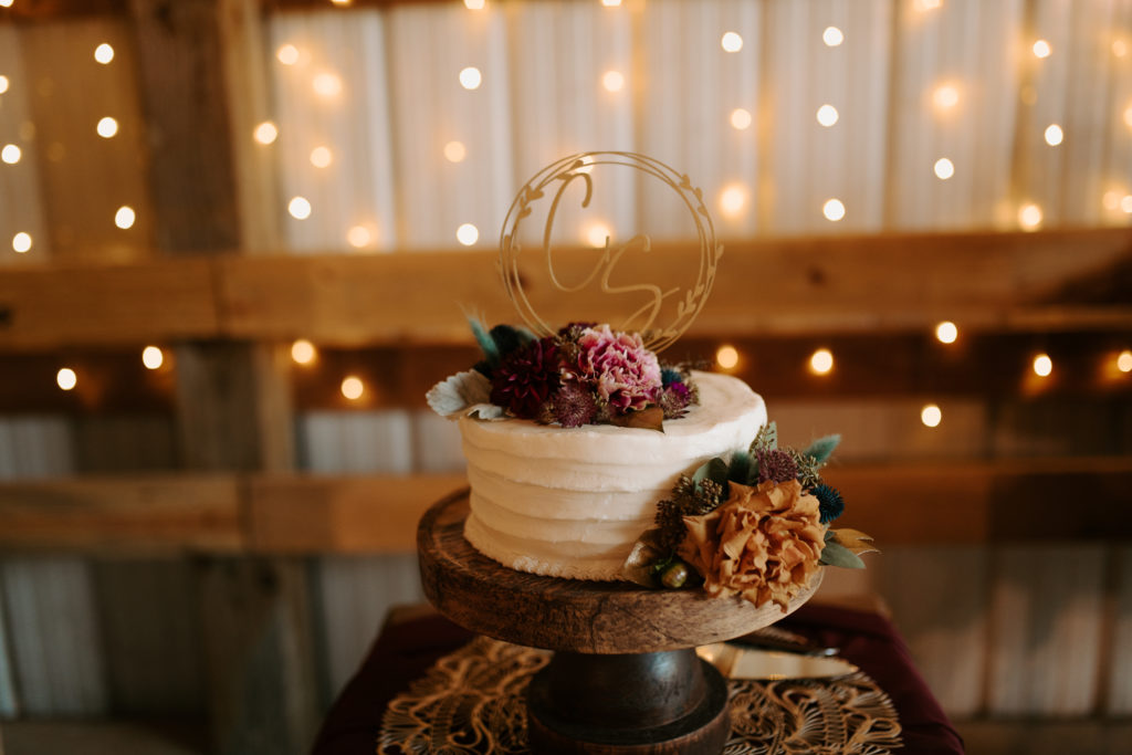 Simple, boho wedding cake with teal and burgundy florals and white icing