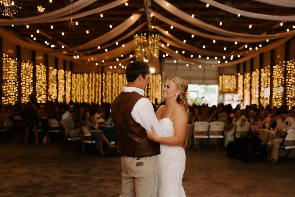 first dance with bride and groom in barn with twinkle lights
