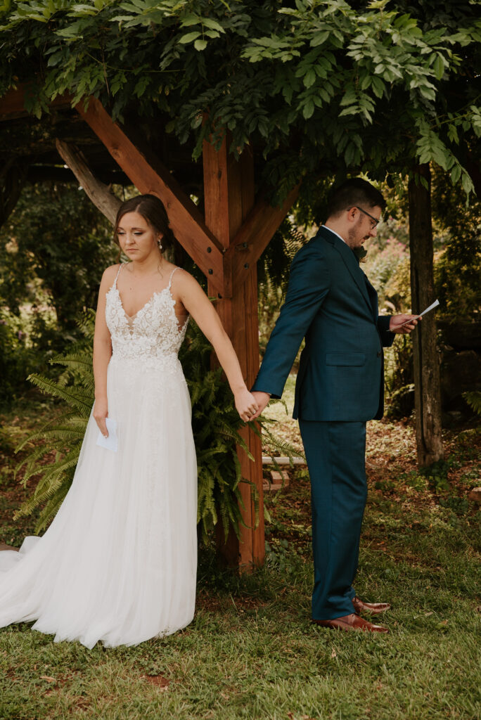 intimate first touch with groom reading personal vows and holding hands around the arbor at old mill farm venue in bedford, virginia