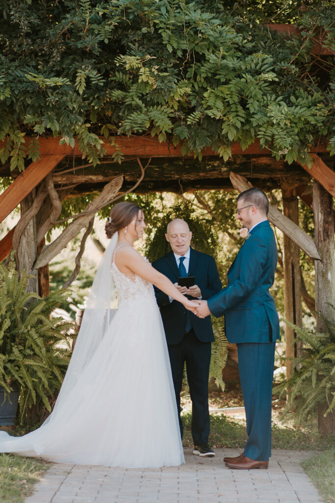 bride and groom exchanging vows under an arbor with luscious greenery at old mill farm venue in bedford, virginia