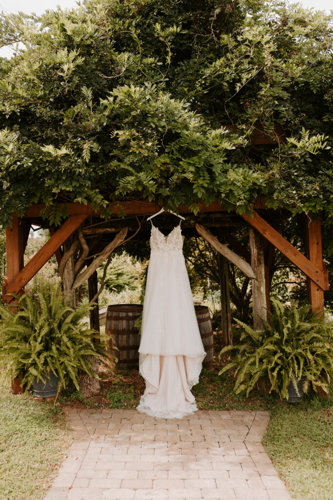 lace wedding dress hanging up in the garden on an arbor at old mill farm in bedford, virginia