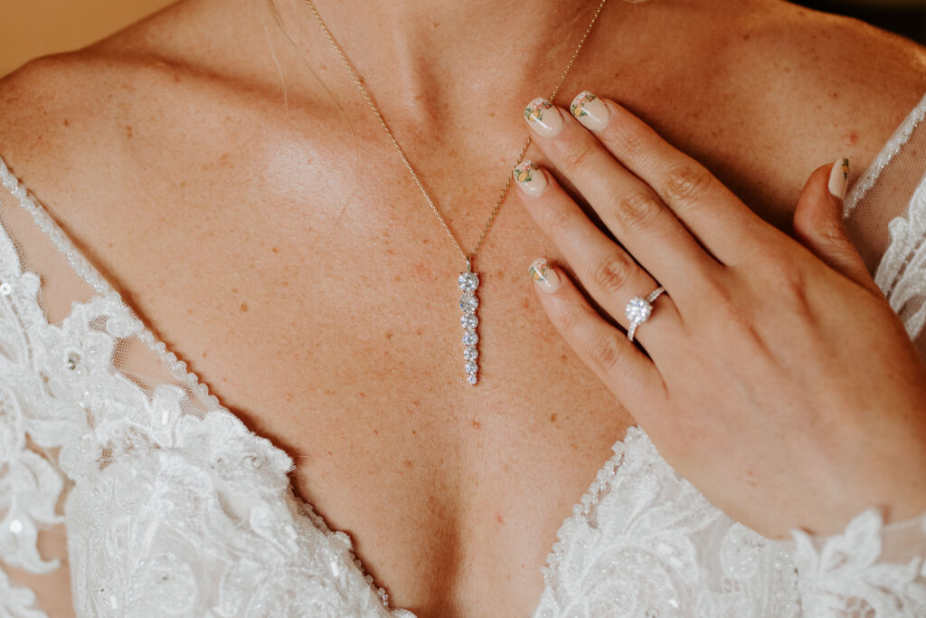 long diamond wedding necklace with the bride's hand showing off her nude, floral nails