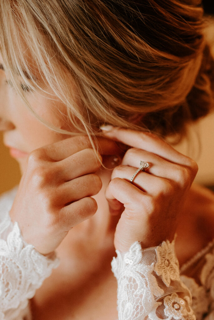 bride putting on her earrings with natural light shining in the room
