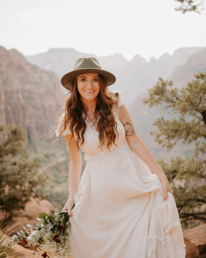 bride holding up her boho dress while walking across red dirt at Zion National Park