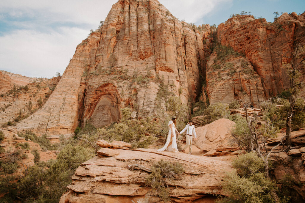 groom leading his bride across red rocks after their Zion National Park Elopement