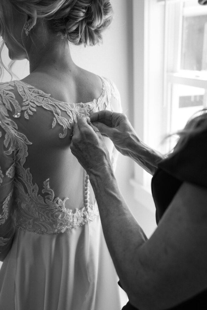 mom buttoning up the bride's dress in the bridal suite