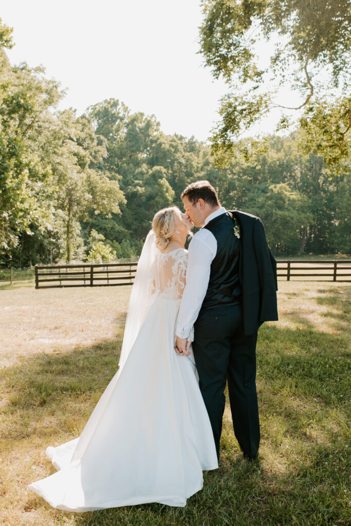 bride and groom share a kiss while holding hands. groom holding his suit jacket over his shoulder.