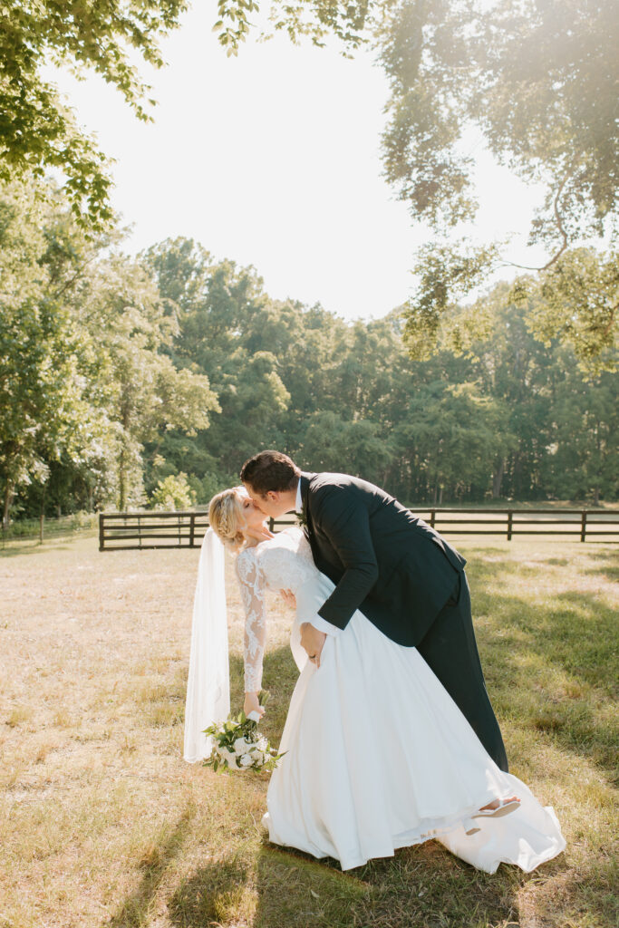 groom dips his bride and goes in for a kiss underneath the trees