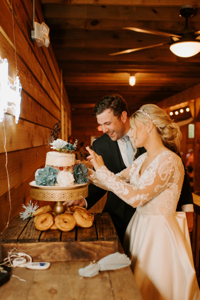 bride and groom cutting their wedding cake in front of their neon sign with their last name