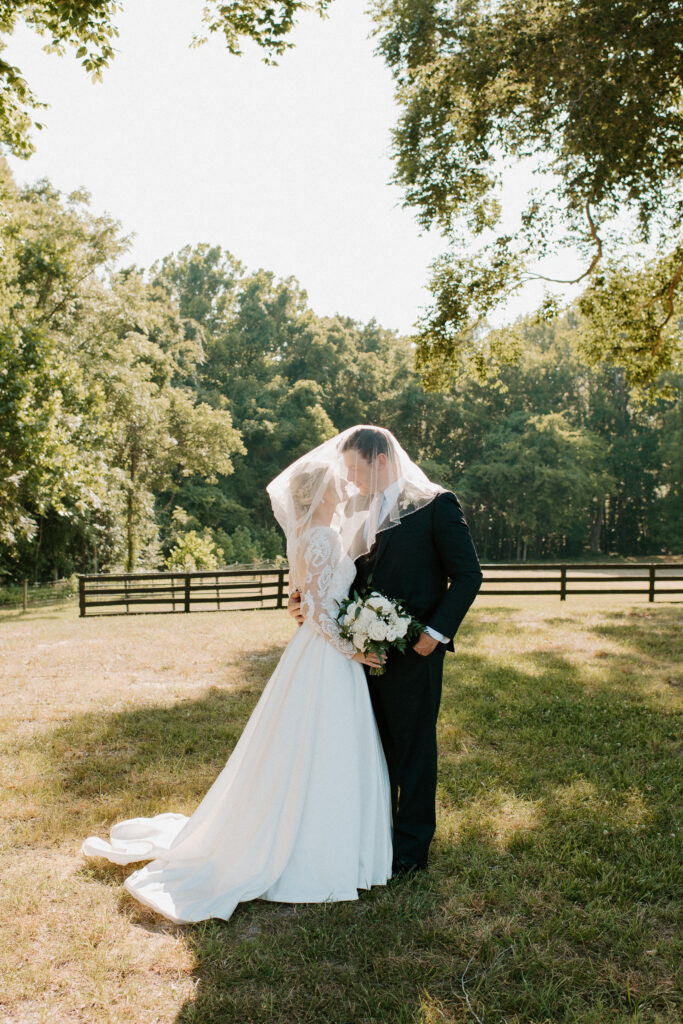 bride and groom snuggle close under the veil while the evening light glows behind them