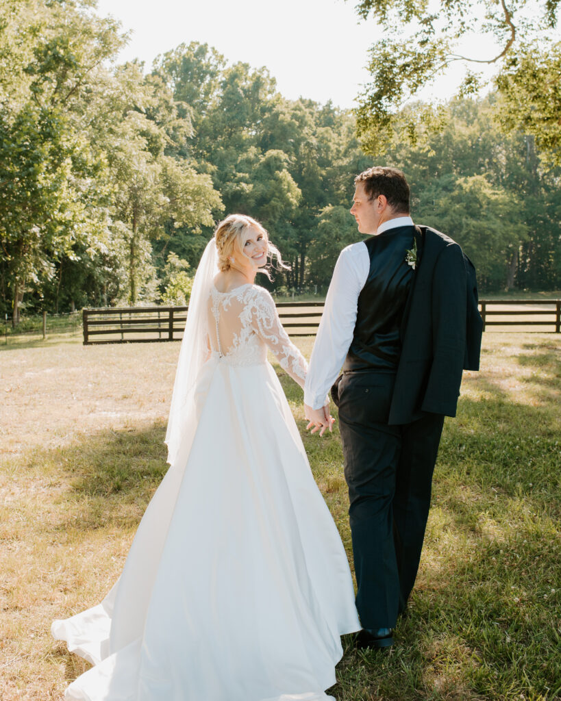 bride looking back as they walk away. groom has his suit jacket thrown over his shoulder