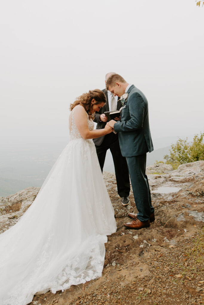 bride and groom holding hands as the officiant says a prayer in the rain over their marriage